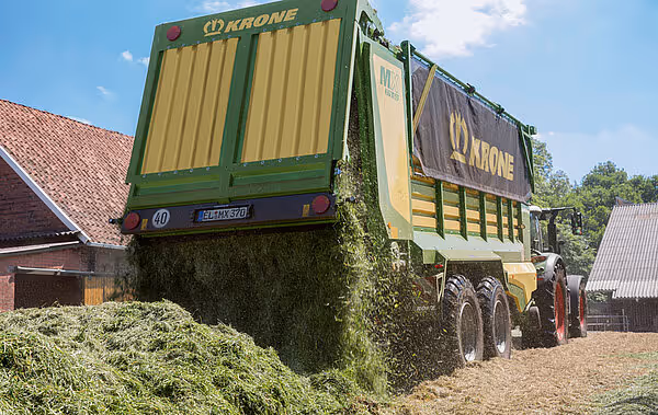 KRONE MX fôrvogn lastet med ensilasje på gård, viser vognen fra siden under fylling.