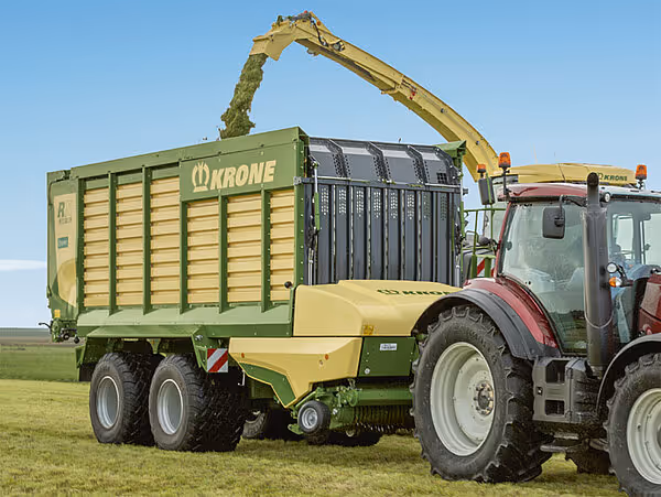 Rød traktor med frontlaster fyller grønn og gul Krone MX silofyll-vogn med hakket fôr.