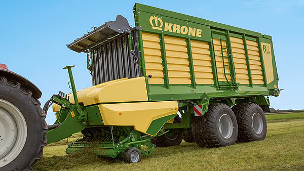 Grønn og gul Krone MX silofôrvogn med åpnet utleveringskjerm på en grønn plen.