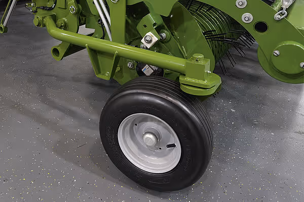 Nærbilde av et enkelt hjul med svart dekk og sølvfarget felg montert på en grønn skafthenger.