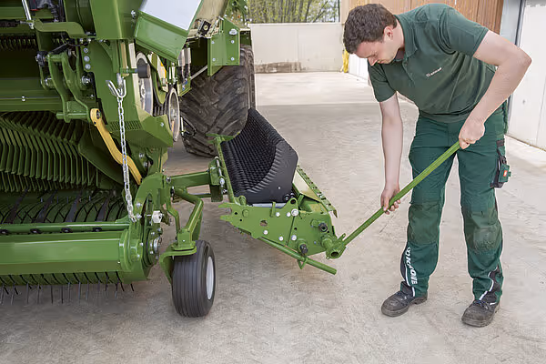 Landbruksarbeider justerer en grønn KRONE RX høstmaskin med en innstillingsverktøy på betongflate.