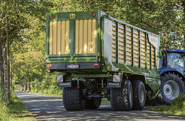KRONE RX silofyll med gult og grønt utseende montert på traktor i dyrkingsområde med trær.