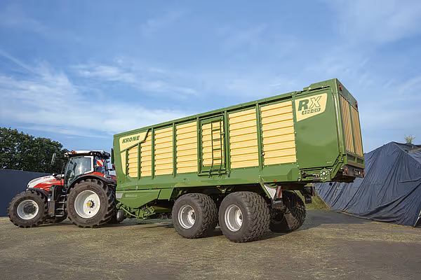 KRONE RX silofyll i gult og grønt montert på traktor på landbruksområde med presenning i bakgrunnen.