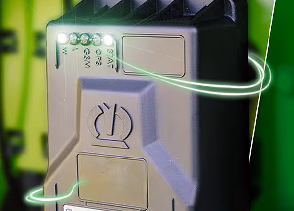 Tett bilde av elektronisk styringsenhet montert på grønn maskin, med grønn lysende kabel og kontaktpunkter.