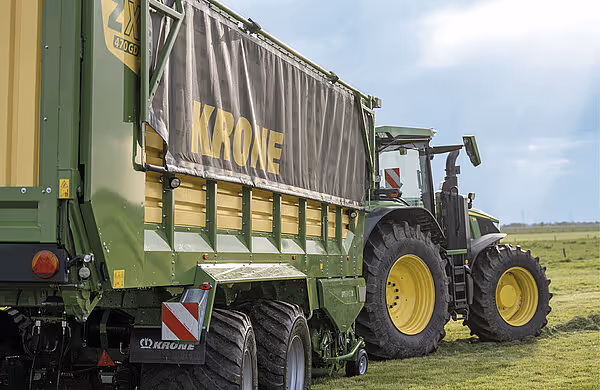 KRONE RX ladjevogn blir lastet med høy ved hjelp av en John Deere traktor med greiparm under høsting.
