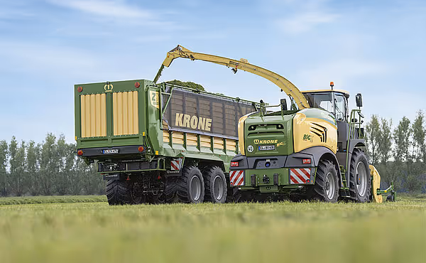 KRONE RX hakkemaskin på lastebil samler og hakker silasje fra åkeren i en grønn innsamlingsvogn.