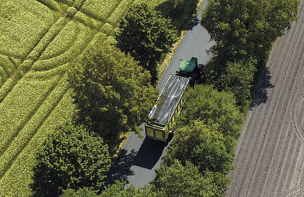 Luftfoto av KRONE RX silasjetransport som kjører inn mellom vegetasjon langs en vannkanal.