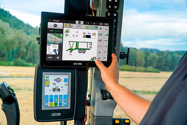 Operatør holder JCB-styringsdisplay som viser kartvisning og kontrollpanel for KRONE RX-maskineri.