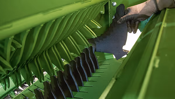 Hånd som justerer kammene på innmatingsmekanismen til KRONE VariPack Plus rundballpresse.