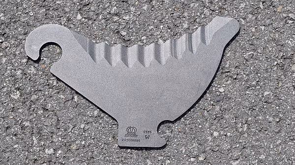 Reservekniv til KRONE VariPack Plus rundballpresse liggende på asfalt, med sagget egg og monteringshull.