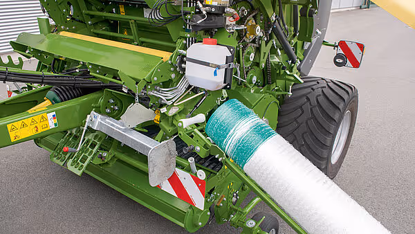 KRONE Varipack Plus rundballepresse med nettrulle montert på sida av maskina. Pressa er utstilt på eit grått golv innandørs.