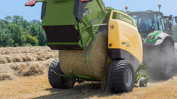 KRONE VariPack rundballpresse i arbeid på åker, produserer rundball av høy med grønt nett.