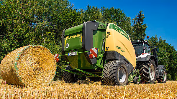 Krone Varipack Plus rundballpresse i arbeid på kornstubber med ferdig rundball. Maskinen er koblet til traktor og produserer store rundaller av halm.