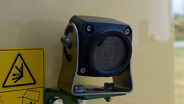 Kamera montert på Krone Varipack Plus rundballpresse for overvåkning under drift. Kameraet er beskyttet med robust svart housing og festet til maskinrammen.