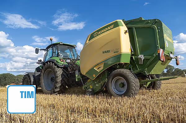 KRONE VariPack pluss ballepresser koblet til grønn traktor arbeider på stubbåker under blå himmel.