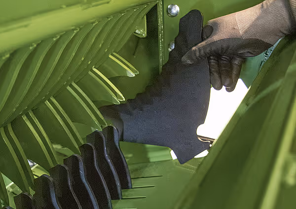 En person med svarte hansker justerer eller vedlikeholder innvendige komponenter på en grønn KRONE Varipack Pro rundballpresse.