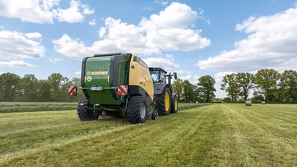 KRONE Varipack Pro rundballpresse i arbeid på en grønn eng under delvis skyet himmel.