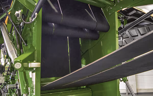 Grønn rundballpresse med svarte transportbelter og grønn ramme, viser den indre mekanismen for ballforming.