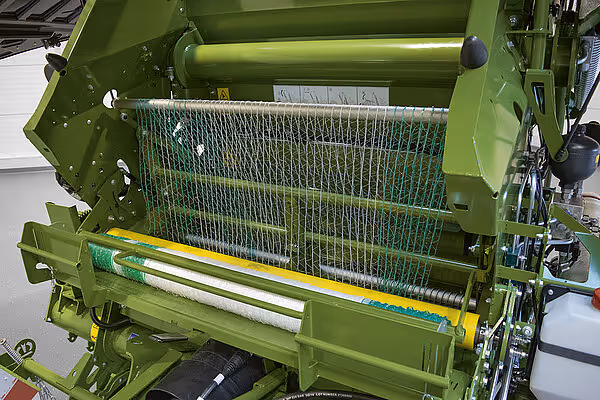 Grønn nettvikling med gul og grønn nettrulle montert i rundballpressen for omsveipning av baller.