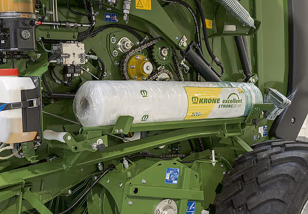 Hvit plastfolie på rullebrakett montert på grønn KRONE rundballpresse for silasjeballproduksjon.