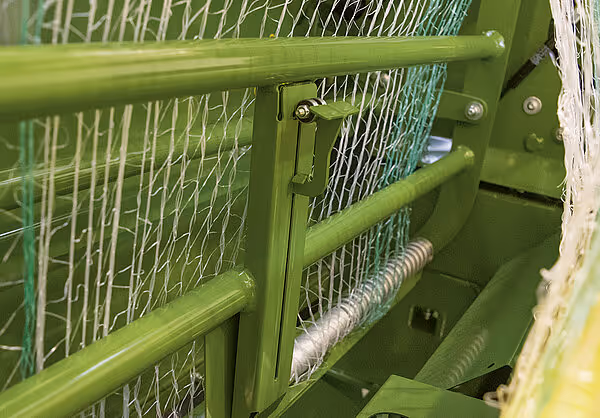 Grønn nettingkassett på KRONE VariPack Pro rundballpresse med synlig fjærmekanisme og nettingtråd. Kassetten er montert på siden av maskinen.