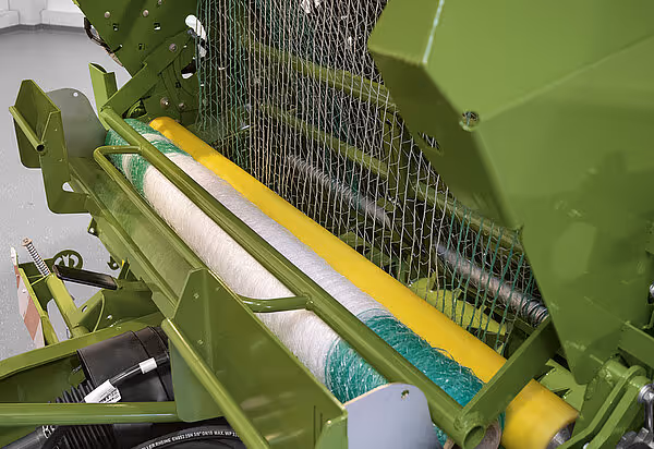 Detaljbilde av foliesystem på KRONE VariPack Pro med hvit plastfolie og gul støttevalse. Nettingkassett er synlig i bakgrunnen.