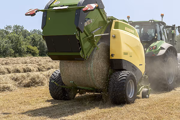 KRONE VariPack Pro rundballpresse i arbeid på stubåker, med grønn traktor som trekker maskinen. Støv virvles opp under pressingen.