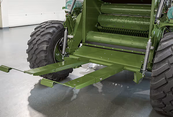 Detaljbilde av understell og pakkekammer på grønn KRONE Varipack Pro rundballpresse. Maskinen står på glatt gulv innendørs.