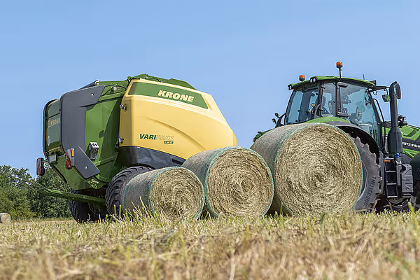 KRONE Varipack Pro rundballpresse på kornstubbing med tre ferdigproduserte rundball plassert ved siden av traktoren. Maskinen har stoppet opp for å vise resultatet.