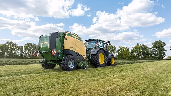 Grønn og gul KRONE VariPack Pro rundballpresse trukket av traktor på grønt jorde under skyet himmel.
