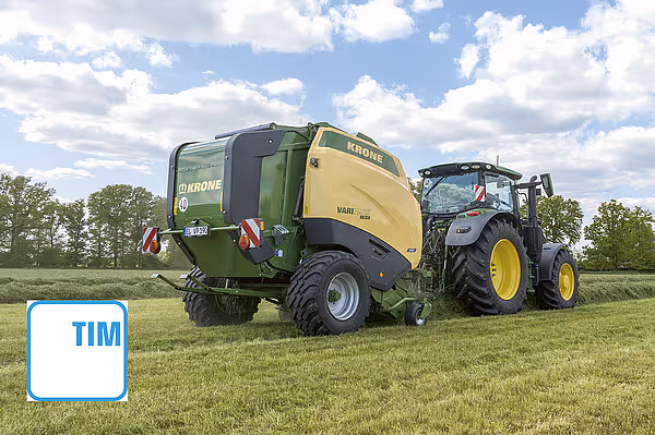 KRONE VariPack Pro rundballepresse koblet til traktor som arbeider på eng under skyet himmel.