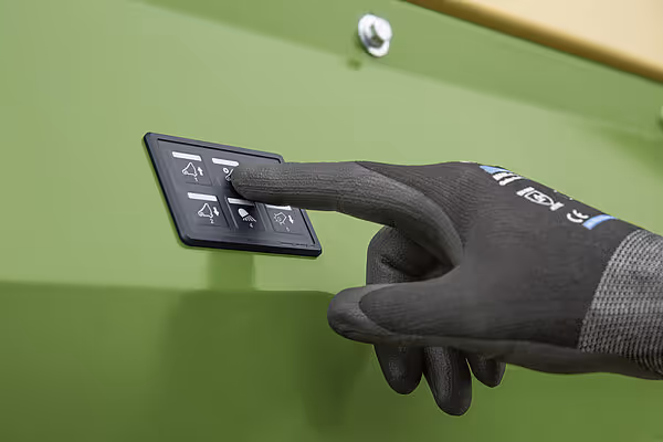 Betjeningspanel på Krone ZX med funktjonskontroller for presseprosessen, operatør har arbeidshandske på.