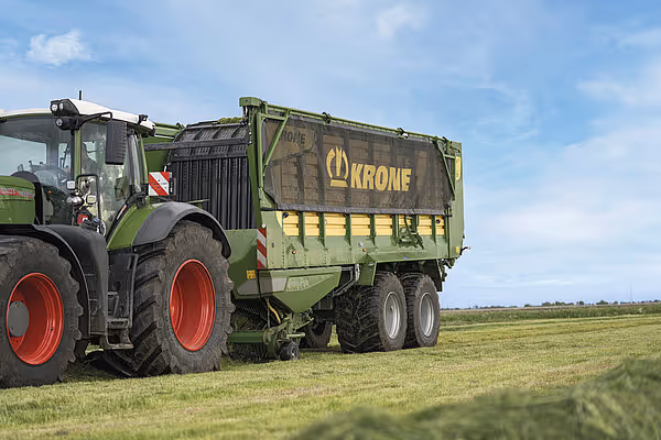KRONE ZX silokjerre med åpen fyllingsluke blir transportert av traktor på grønt beiteområde.