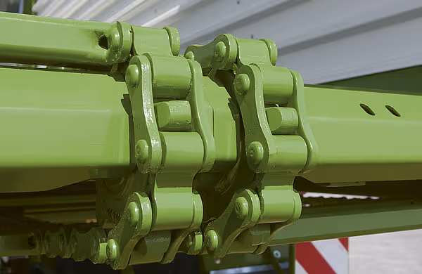 Nærbilde av doble ledekjedekoblinger i grønt stål på høstevognens matorsystem.