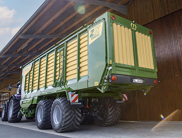 Grønn KRONE ZX-vogn med åpne høylaster-sider parkert under tak, sett fra siden med kraftige dekk og grønn ramme.