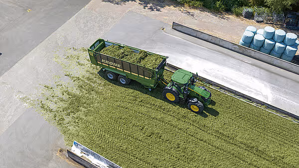 Flyfoto av grønn KRONE ZX-vogn trukket av grønn traktor på eng, sett ovenfra.