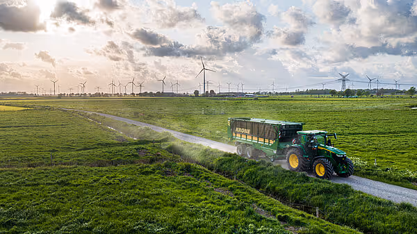 Traktor med grønn KRONE ZX silofôrforvogn kjøring på landsvei i landbrukslandskap.