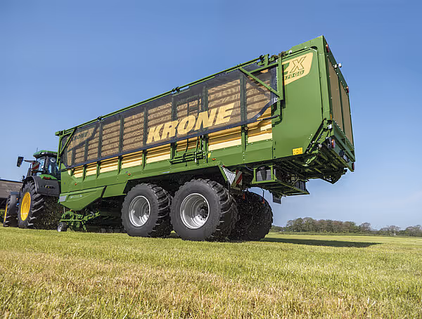 KRONE ZX vogn med grønt og gult design trukket av John Deere traktor på åpen åker med påkjørte sidelister.