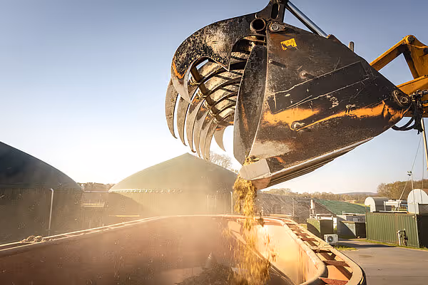 En mekanisk lasteløffel fyller silage fra en traktor ved soloppgang på en gård.