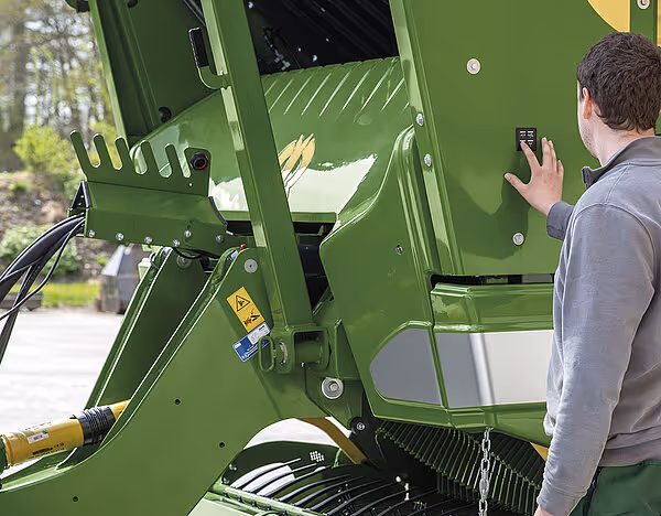 Mann inspiserer åpen dør på førerkabinen på grønn KRONE rotorveihakker.