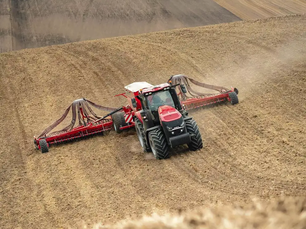 En Case IH Magnum-traktor med en stor såmaskin arbeider i en åker, sett ovenfra, mens den sår i tørr jord.