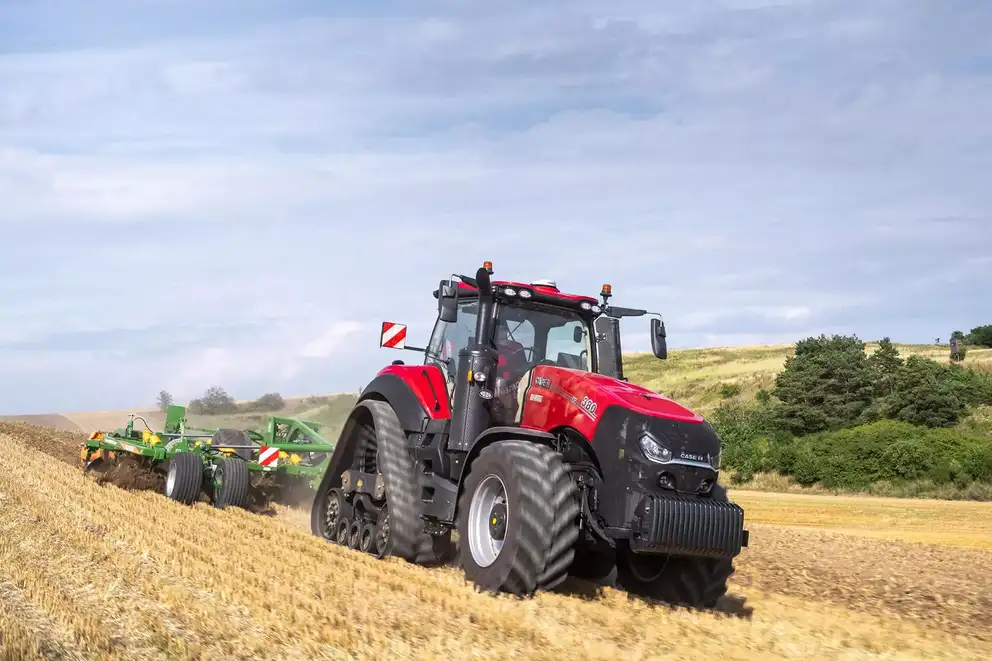 En Case IH Magnum-traktor arbeider på en åker med skrånende landskap, med skog og åser i bakgrunnen.