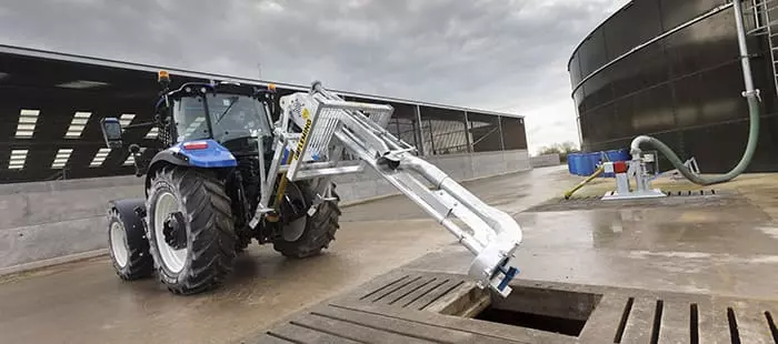 New Holland-traktor med frontlaster – En blå New Holland-traktor bruker en frontlaster til å håndtere materialer på en gård.