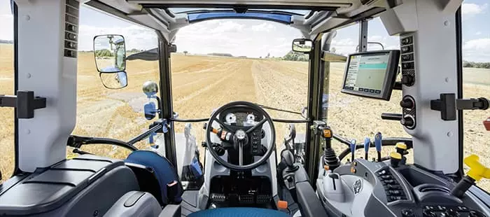 Førersete i New Holland-traktor – Komfortabelt blått sete med armlener inne i førerhuset på en New Holland-traktor.