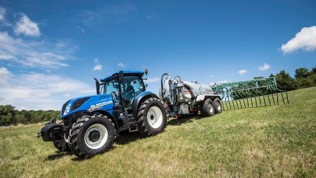 New Holland T7.265 S-traktor koblet til en Joskin-vogntank, parkert foran en biogassanlegg eller silo.