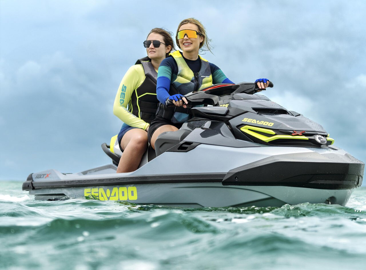 To personer kjører en Sea-Doo RXT-X RS 325 i Ice Metal & Manta Green fargekombinasjon på åpent vann, iført våtdrakter og redningsvester.