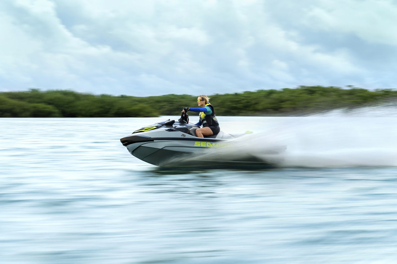 Kvinne kjører en Sea-Doo RXT-X RS 325 i høy hastighet over vannet, med en dramatisk bevegelseseffekt som viser kraften i 325 hk-motoren.