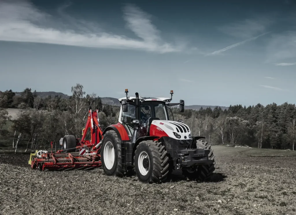 En Steyr 6280 Absolut CVT traktor på en åker med en kultivator, fotografert fra lav vinkel.