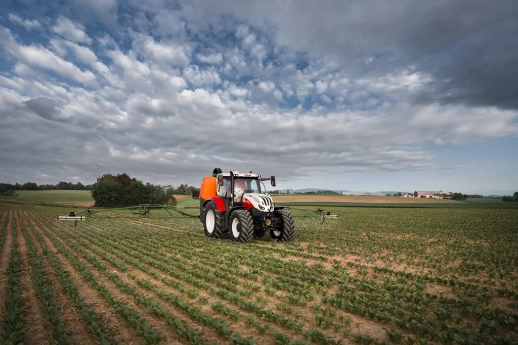 En Steyr-traktor med påmontert sprøyteutstyr jobber på en åker.