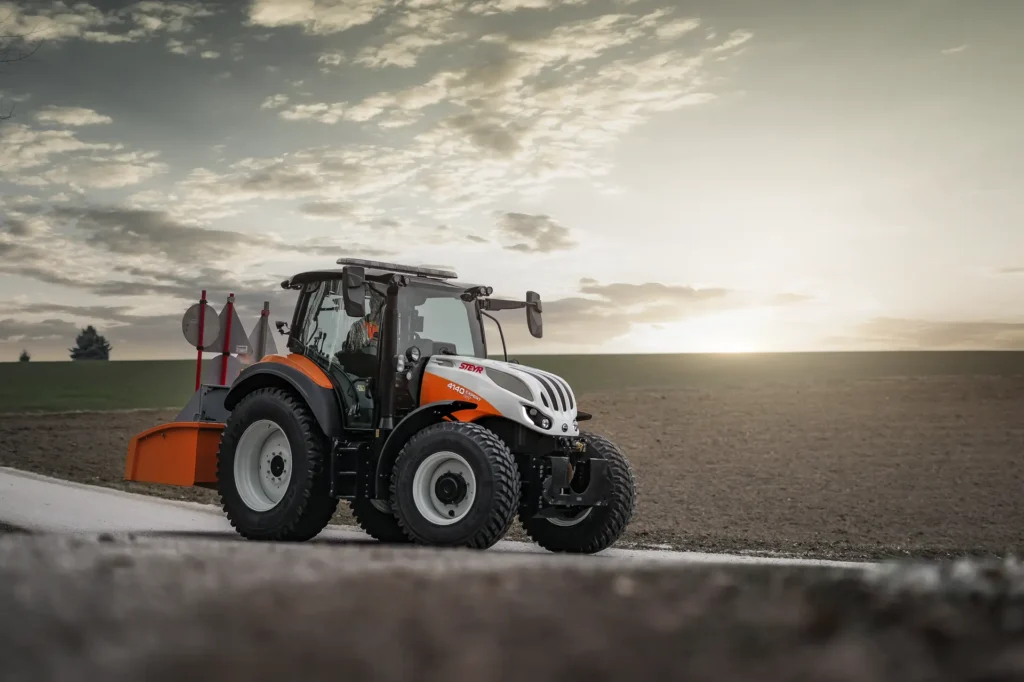 En Steyr 4140 Expert CVT traktor med plog på en landevei i solnedgangen.